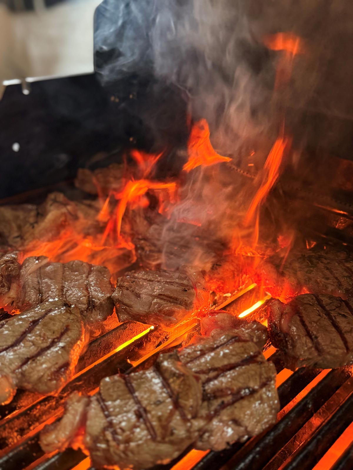 Mehrere saftige Steaks werden auf einem Grill mit leuchtenden Flammen gegrillt