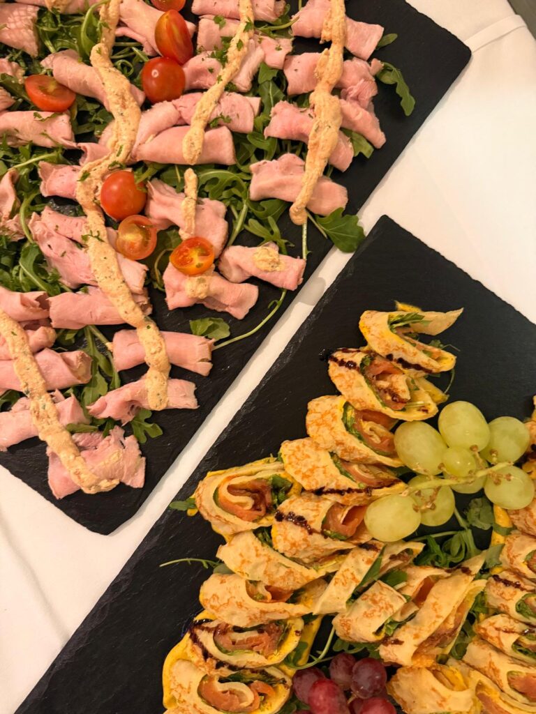 Zwei Schieferplatten mit Fleischroellchen Tomaten Pfannkuchenroellchen und Trauben